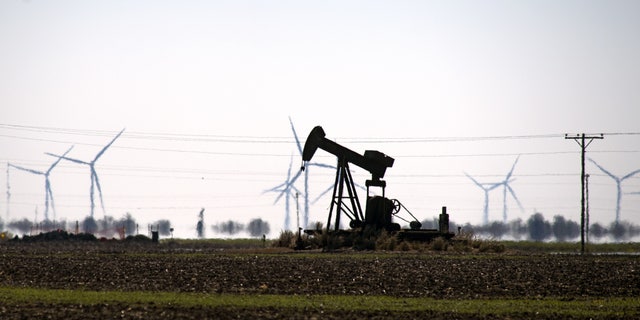 An oil pump jack in a field with wind turbines in Corpus Christi, Texas, Feb. 19, 2021. 