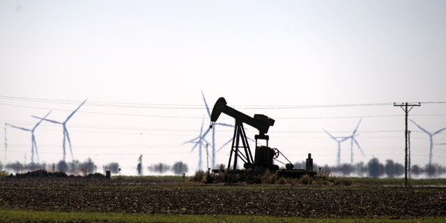 An oil pump jack in a field with wind turbines in Corpus Christi, Texas, Feb. 19, 2021. 