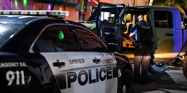 A Miami Beach police officer inspects the inside of a car on Ocean Drive in Miami Beach, Florida, on March 22, 2021.