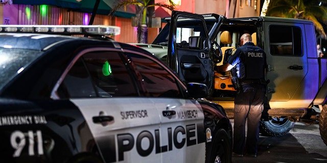 A Miami Beach police officer inspects the inside of a car on Ocean Drive in Miami Beach, Florida, on March 22, 2021.