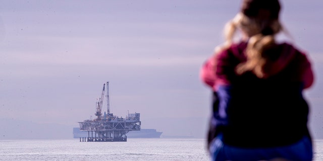 \A person looks out over the ocean with a view of oil platform Esther and container ships off the coast of Seal Beach, California, on Thursday, Dec. 16, 2021.  (Allen J. Schaben / Los Angeles Times via Getty Images)