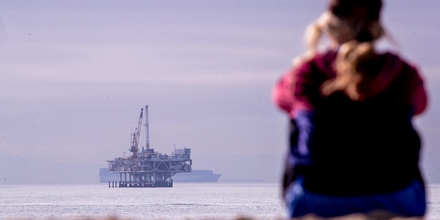 \A person looks out over the ocean with a view of oil platform Esther and container ships off the coast of Seal Beach, California, on Thursday, Dec. 16, 2021.  (Allen J. Schaben / Los Angeles Times via Getty Images)