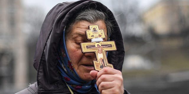 Религиозная женщина держит крест во время молитвы на площади Независимости в Киеве утром 24 февраля 2022 года.