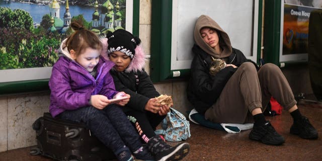 Лия (слева) и Жасмин разговаривают по телефону, когда вместе с родителями прячутся на станции в центре Киева, 24 февраля 2022 года.