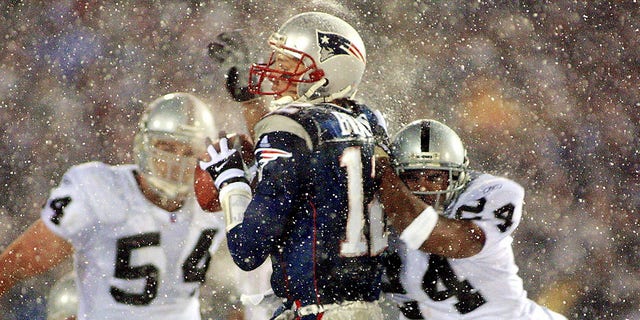 New England Patriots quarterback Tom Brady (C) takes a hit from Charles Woodson (R) of the Oakland Raiders on a pass attempt in the last two minutes of the game in their AFC playoff 19 January 2002 in Foxboro, Massachusetts.  The Patriots won 16-13 in overtime.