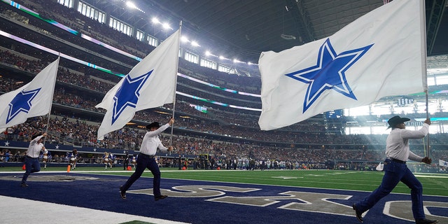 Dallas Cowboys cheerleaders taking the field with flags in Arlington, Texas, in November 2017.