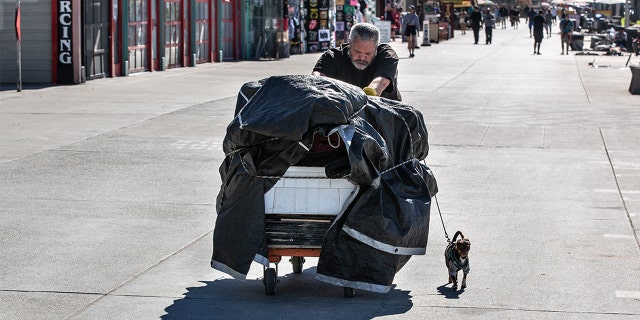 FILE – A homeless man pushes a cart with his belonging along the Boardwalk in this beach community adjacent to Santa Monica on February 7, 2022, in Venice Beach, Kalifornië.
