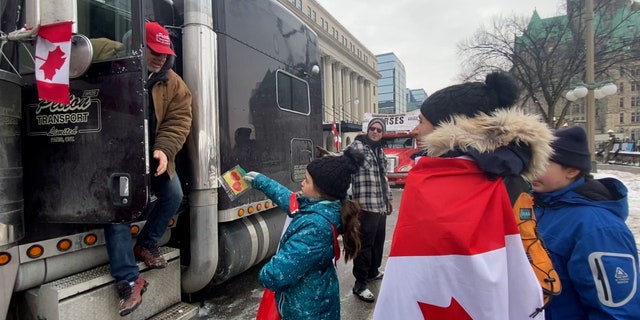 A girl and her family walk through the line of truckers, handing out thank you notes