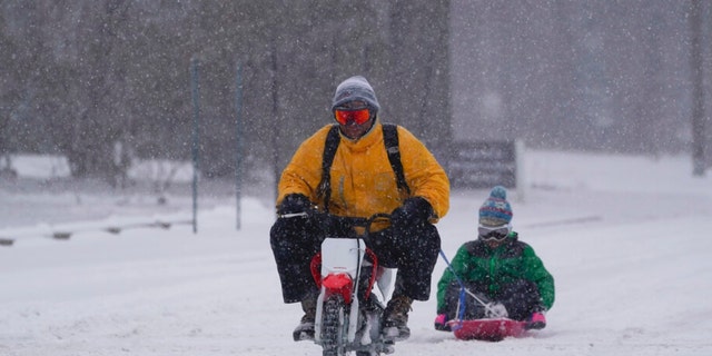 Adam Basch pulls Lim Walthall on his sled, Thursday, Feb. 3, 2022, in Indianapolis. A major winter storm with millions of Americans in its path is spreading rain, freezing rain and heavy snow further across the country.