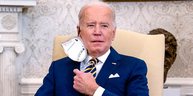 President Joe Biden removes his protective face mask before speaking during a meeting with the Qatar's Emir Sheikh Tamim bin Hamad Al Thani in the Oval Office of the White House, Monday, Jan. 31, 2022, in Washington. 