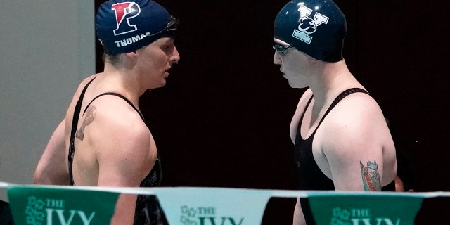 Penn's Lia Thomas, 剩下, leaves the pool deck as Yale's Iszac Henig, 对, prepares to swim in a qualifying heat of the 100-yard freestyle at the Ivy League Women's Swimming and Diving Championships at Harvard University, 星期六, 二月. 19, 2022, in Cambridge, 弥撒.