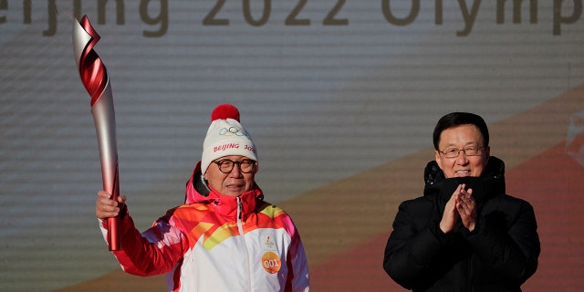 First Torch bearer Luo Zhihuan holds up the torch after receiving it from Chinese Vice Premier Han Zheng before the start of the torch relay for the 2022 Winter Olympics at the Olympic Forest Park in Beijing on Wednesday, Feb. 2, 2022.