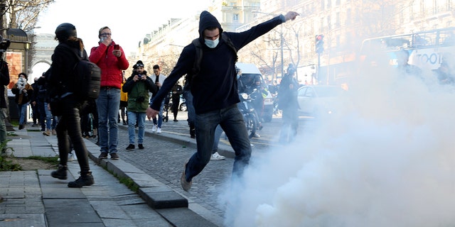 A demonstrator kicks at a tear gas grenade during a protest on the Champs-Élysées avenue, Saturday, Feb.12, 2022, in Paris. 