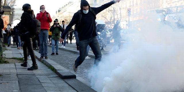 A demonstrator kicks at a tear gas grenade during a protest on the Champs-Élysées avenue, Saturday, Feb.12, 2022, in Paris.