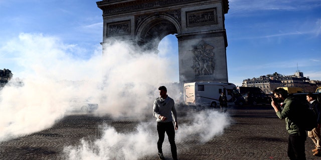 A man walks through tear gas on the Place Charles De Gaulle in Paris Feb. 12, 2022, as convoys of protesters,