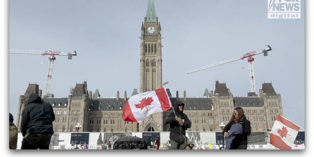 A man waves a Canadian flag from a hockey stick in front of the Canadian Parliament building during the Freedom Convoy 2022.