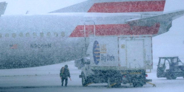 Snow falls on a ground crew working outside a parked plane at Dallas Fort Worth International Airport in Grapevine, Texas, Thursday, Feb. 3, 2022.  The historic freeze covered the Lone Star State and left millions without power. (AP Photo/LM Otero)