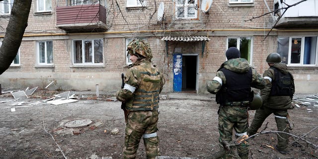 Militants of the self-proclaimed Donetsk People's Republic stand in front of an apartment building, which locals said was damaged by recent shelling, in the separatist-controlled town of Yasynuvata (Yasinovataya) in the Donetsk region, Ukraine February 24, 2022.