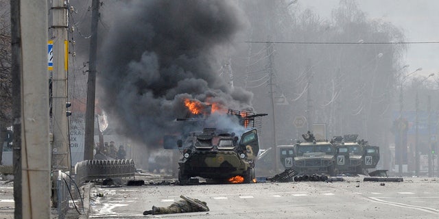 Un véhicule blindé de transport de troupes (APC) russe brûle à côté du corps d'un soldat non identifié lors d'un combat avec les forces armées ukrainiennes à Kharkiv.