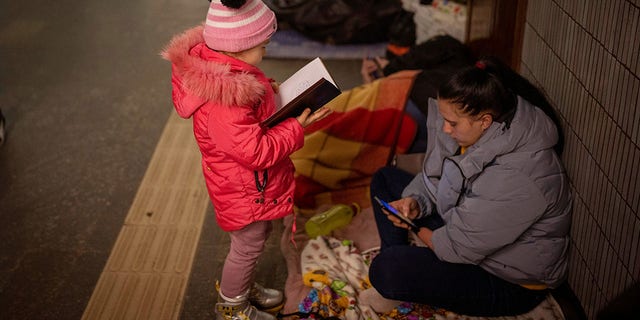 A girl looks at a notebook next to her mother as they stand in the Kyiv subway, using it as a bomb shelter, in Ukraine, on Saturday, Feb. 26, 2022.