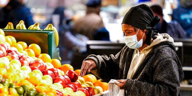 A shopper waring a proactive mask as a precaution against the spread of the coronavirus selects fruit at the Reading Terminal Market in Philadelphia, mercoledì, Feb. 16, 2022.