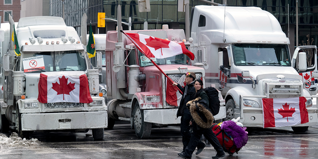 Protesters walk with bags past trucks parked on downtown streets on Wednesday, Feb. 2, 2022, in Ottawa, Ontario. Thousands of protesters railing against vaccine mandates and other COVID-19 restrictions descended on the capital, deliberately blocking traffic around Parliament Hill. 