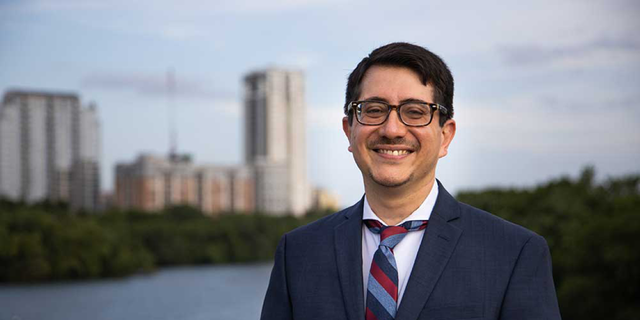 Jose Garza wearing a suit smiling in front of Austin skyline