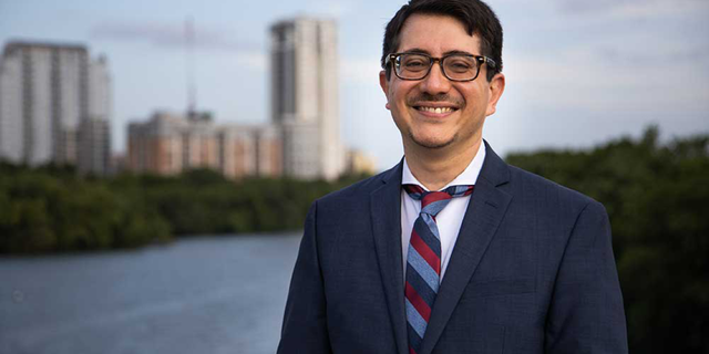 Jose Garza wearing a suit smiling in front of Austin skyline