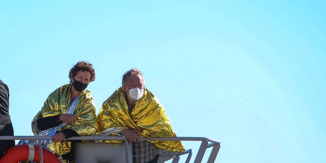 A man and a woman covered with a thermal blankets look out from Greek Navy ship as they arrive at the port of Corfu island, northwestern Greece, following their evacuation from a ferry, Friday, Feb. 18, 2022. 