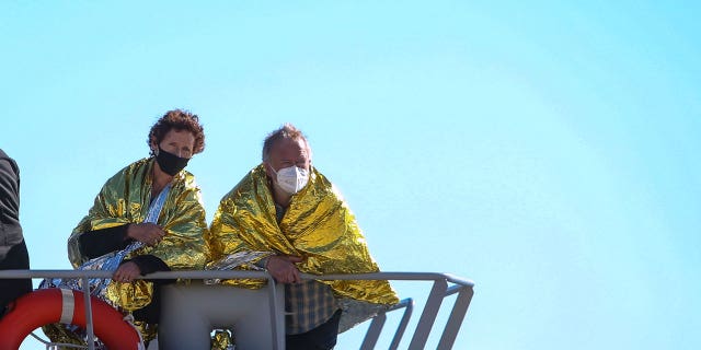 A man and a woman covered with a thermal blankets look out from Greek Navy ship as they arrive at the port of Corfu island, northwestern Greece, following their evacuation from a ferry, Friday, Feb. 18, 2022.