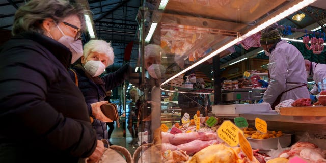 Two elderly women buy food in a market in Florence, Italy, Thursday, Feb. 17, 2022.