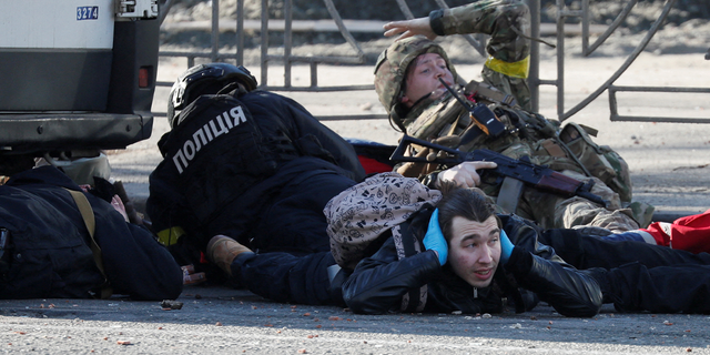 People take cover as an air-raid siren sounds, near an apartment building damaged by recent shelling in Kyiv, Ukraine, on February 26, 2022. 