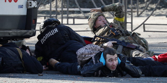 People take cover as an air-raid siren sounds, near an apartment building damaged by recent shelling in Kyiv, Ukraine February 26, 2022.