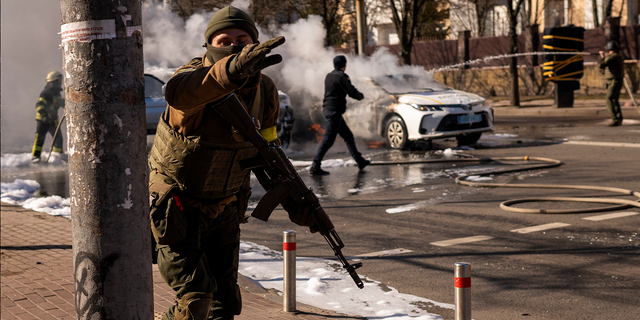 Ukrainian soldiers take positions outside a military facility as two cars burn, in a street in Kyiv, Ukraine, Saturday, Feb. 26, 2022.