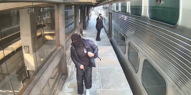 In this surveillance photo, the suspect is seen holding the semi-automatic handgun near his waist while walking down the platform and away from a train conductor who has his hands raised.