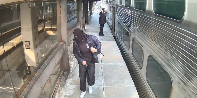 In this surveillance photo, the suspect is seen holding the semi-automatic handgun near his waist while walking down the platform and away from a train conductor who has his hands raised.