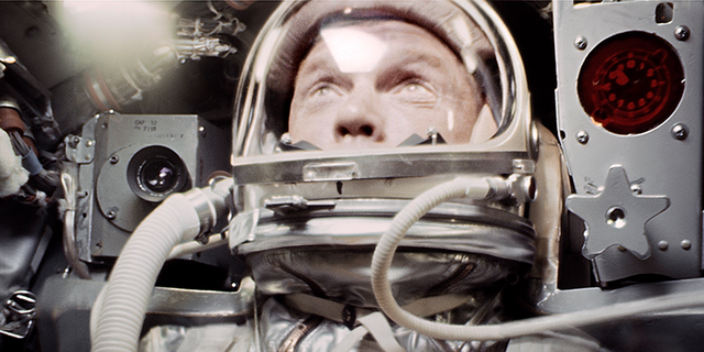 Glenn observes his booster falling away against the curvature of Earth through the capsule window, signifying the moment he had reached orbit.