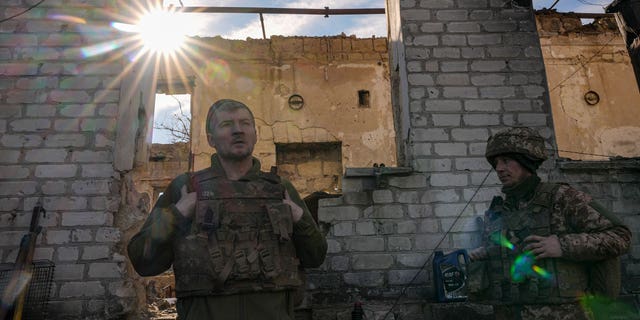Ukrainian soldiers stand next to a destroyed house near the frontline village of Krymsky in eastern Ukraine's Luhansk region, Saturday, February 19, 2022. 