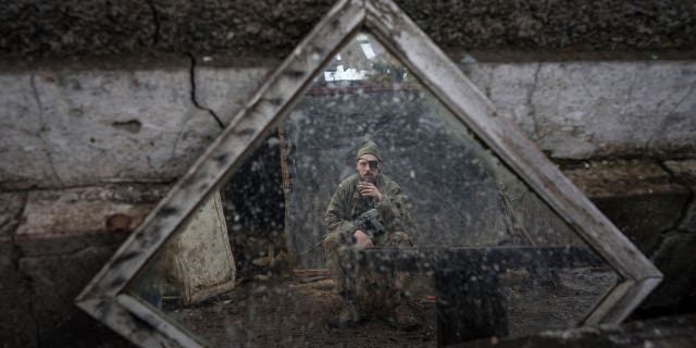 A Ukrainian serviceman is reflected in a mirror as he smokes a cigarette on a position at the line of separation between Ukraine- and rebel-held territory near Zolote, Ukraine, Saturday, Feb. 19, 2022.
