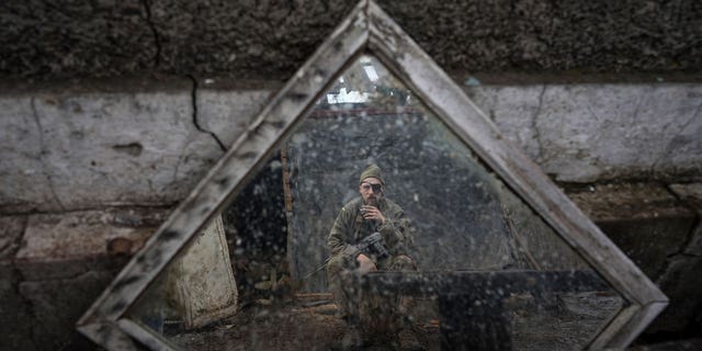 A Ukrainian serviceman is reflected in a mirror as he smokes a cigarette on a position at the line of separation between Ukraine-held territory and rebel-held territory near Zolote, Ukraine, Saturday, Feb. 19, 2022. 
