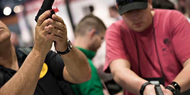 Attendees look over Glock, Inc. pistols on the exhibition floor of the 144th National Rifle Association (NRA) Annual Meetings and Exhibits at the Music City Center in Nashville, Tennessee, April 11, 2015.