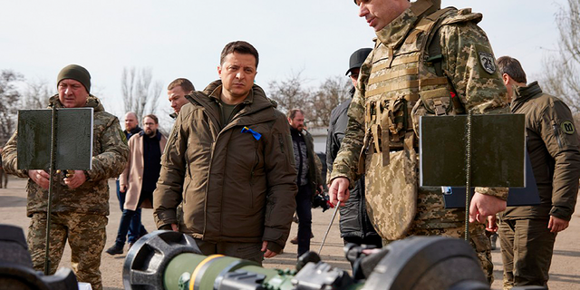 Na této zveřejněné fotografii poskytnuté ukrajinskou prezidentskou tiskovou kanceláří, ukrajinský prezident Volodymyr Zelenskyj, uprostřed, kontroluje zbraně během návštěvy ukrajinské pobřežní stráže v Mariupolu, Doněcká oblast, východní Ukrajina, čtvrtek 17. února 2022.