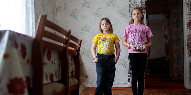 On Feb. 10, 2022, 9-year-old Daryna (right) holds her teddy bear as she stands with her younger sister, Katia, 7, in the dining room of their home in eastern Ukraine.