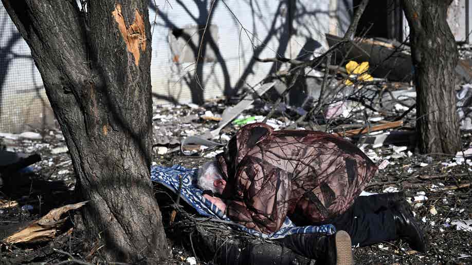 A man reacts at the body of a relative outside a destroyed building after bombings on the eastern Ukraine town of Chuguiv on February 24, 2022