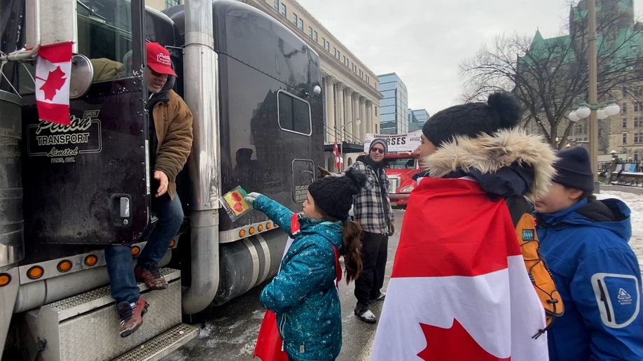 A girl and her family walk through the line of truckers, handing out thank-you notes.