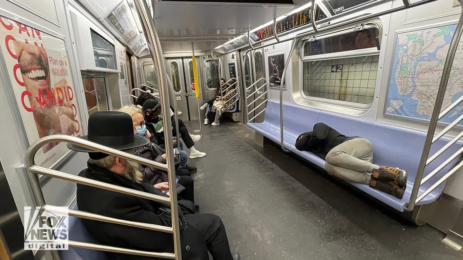 Image shows an individual sleeping in a NYC subway car. 