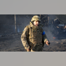 A Ukrainian soldier shows a grenade, near burning military trucks in a street in Kyiv, Ukraine, Saturday, Feb. 26, 2022. Russian troops stormed toward Ukraine's capital Saturday, and street fighting broke out as city officials urged residents to take shelter.