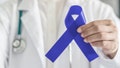 Dark blue ribbon for colon - colorectal cancer awareness on medical doctor's hand support