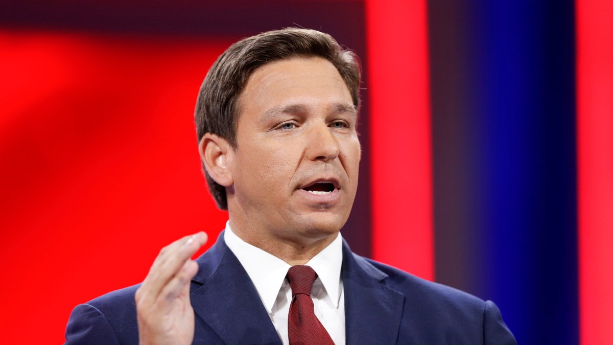 Ron DeSantis in a suit speaking at CPAC in Orlando Florida before a red background