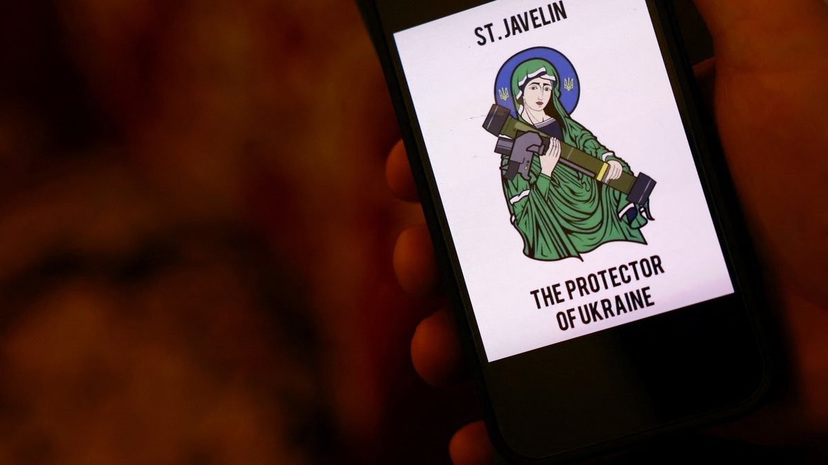 A member of security holds up a mobile phone showing the picture of an icon showing a Saint holding a javelin anti-tank missile in Lviv